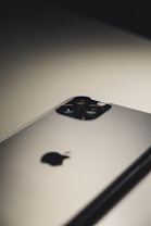 A close-up of a smartphone placed on a flat surface, highlighting its camera module and logo. The lighting creates a soft shadow, emphasizing the sleek design.